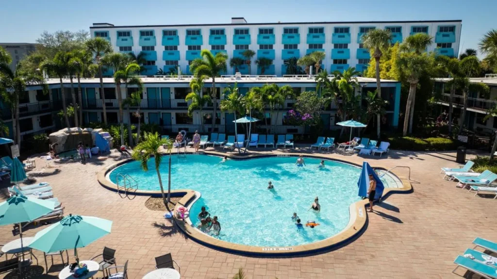 Piscina al aire libre con palmeras y sombrillas de verde azulado frente a CoCo Key Hotel Orlando