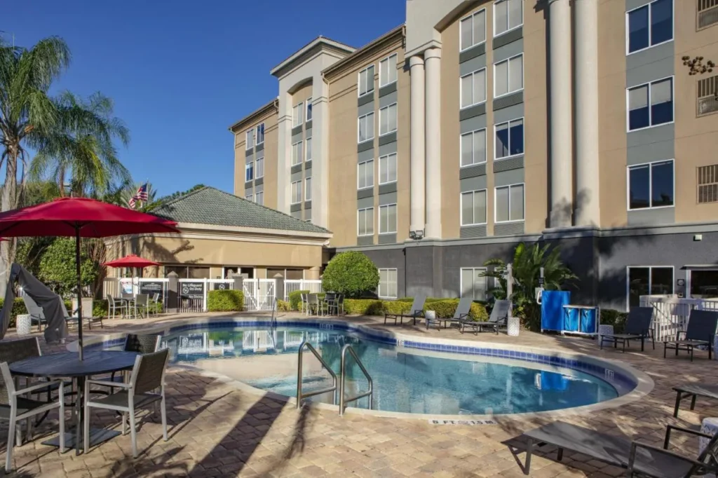 Piscina al aire libre con sombrillas y tumbonas rojas junto al edificio Hampton Inn Orlando/Lake Buena Vista