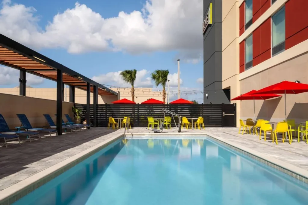 Outdoor pool with red umbrellas and shaded seating at Home2 Suites by Hilton Winter Haven