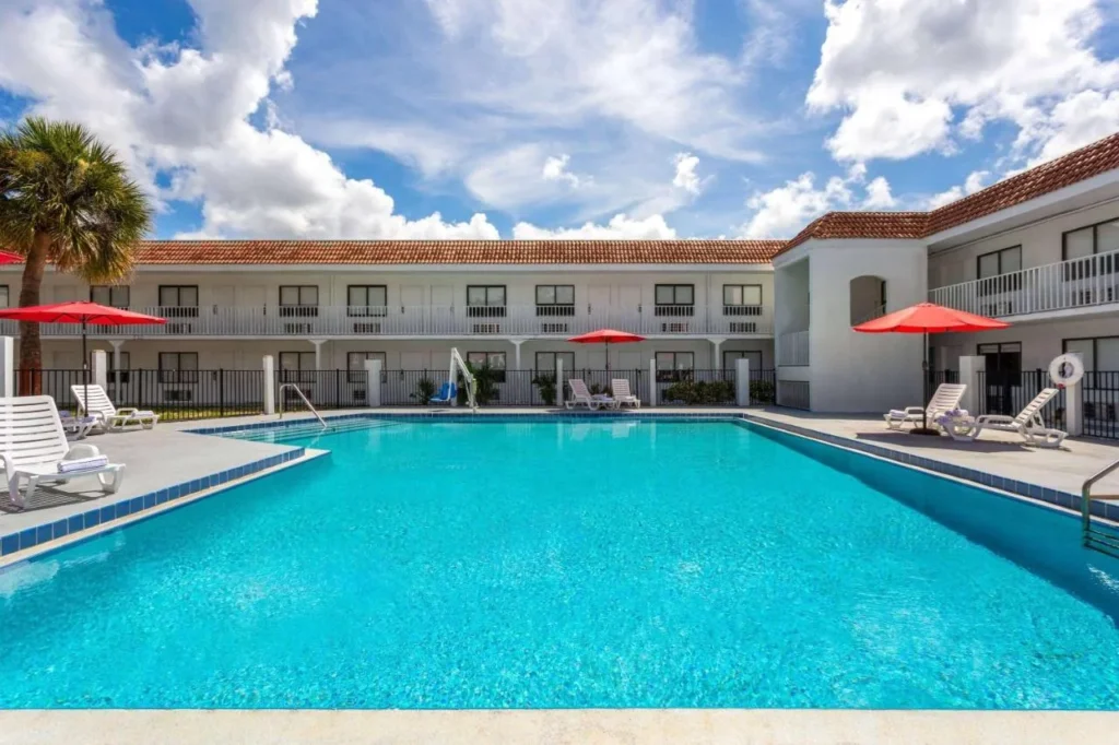 Piscina al aire libre con sombrillas rojas y alas de habitaci&oacute;n de dos pisos en Travelodge Orlando Lake Buena Vista South