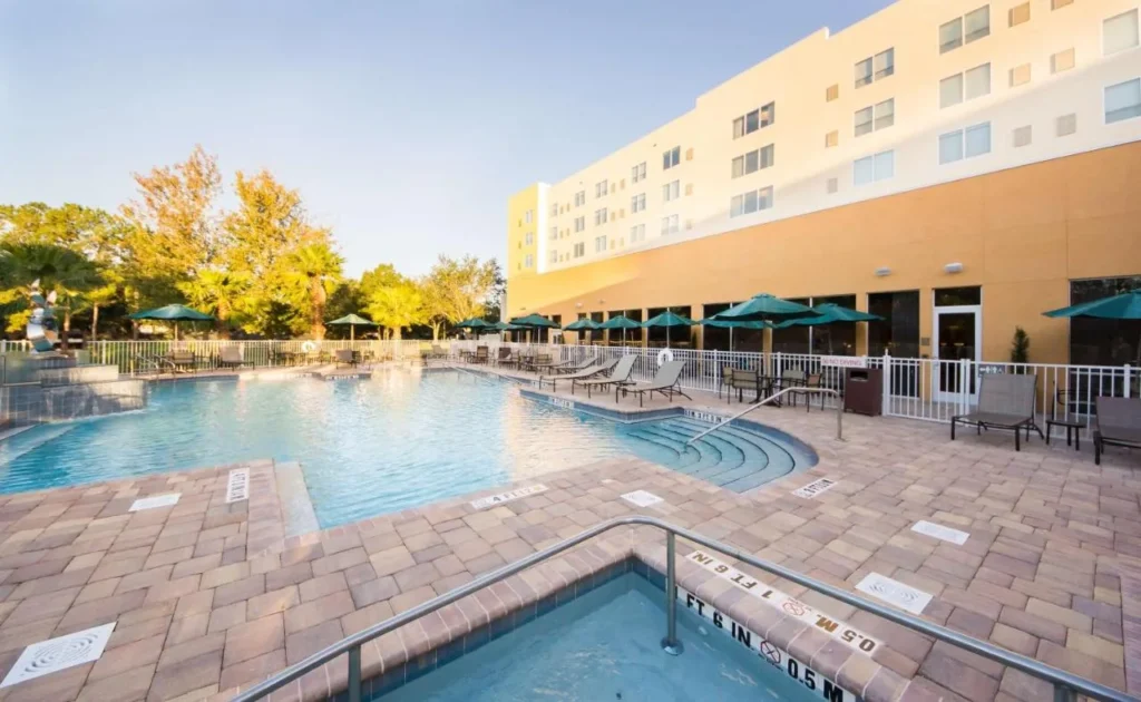 Piscina al aire libre con entrada escalonada, tumbonas y sombrillas verdes en Hyatt Place Orlando/Lake Buena Vista