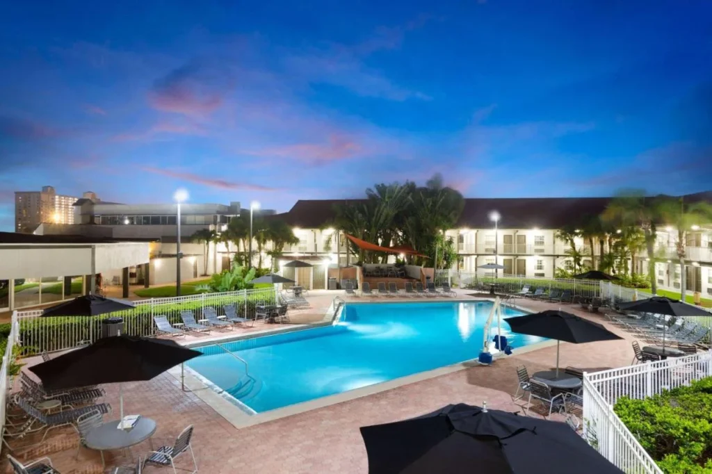 Outdoor pool with umbrellas and lounge chairs at dusk at La Quinta Inn Cocoa Beach-Port Canaveral
