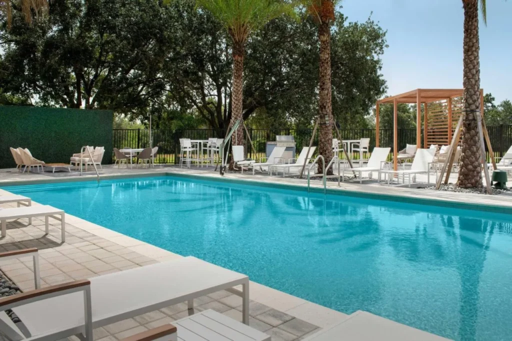 Piscina al aire libre con tumbonas blancas, palmeras y una pérgola en Element Orlando Universal Blvd.