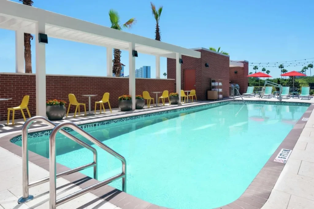 Piscina al aire libre con sillas amarillas, pérgola y parrillas en Home2 Suites Orlando Near Universal