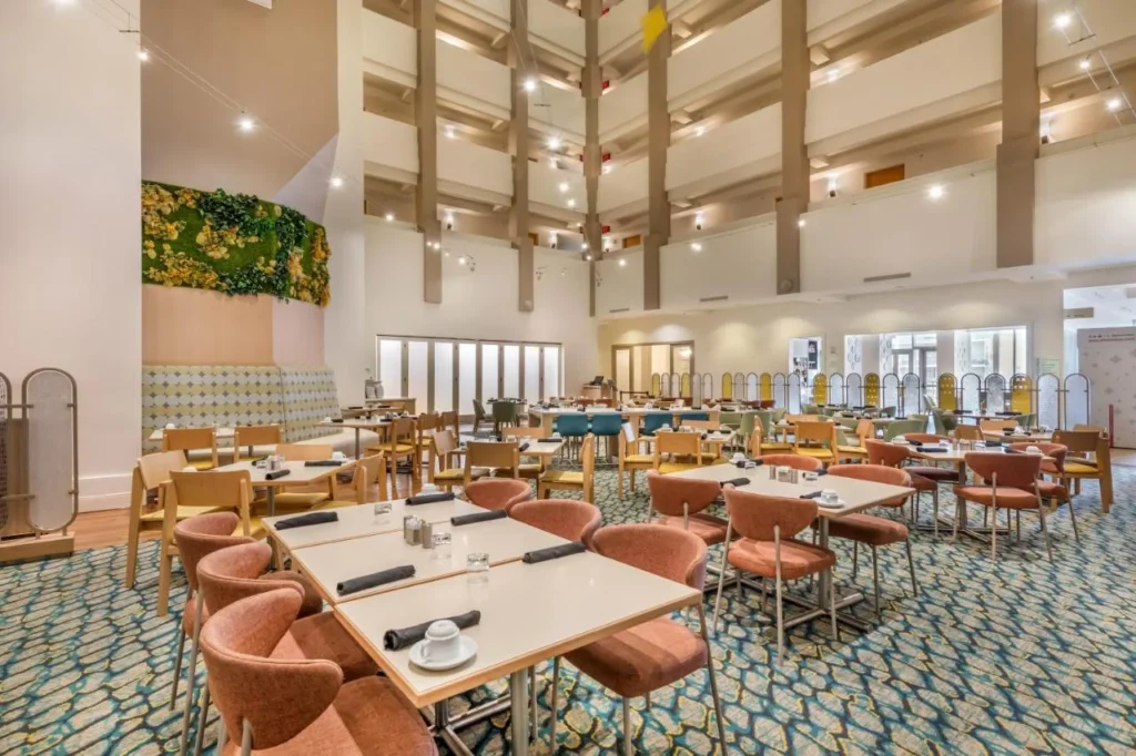 Restaurante Palm Breezes comedor con mesas fijas bajo el alto atrio en Holiday Inn Orlando - Disney Springs &Aacute;rea