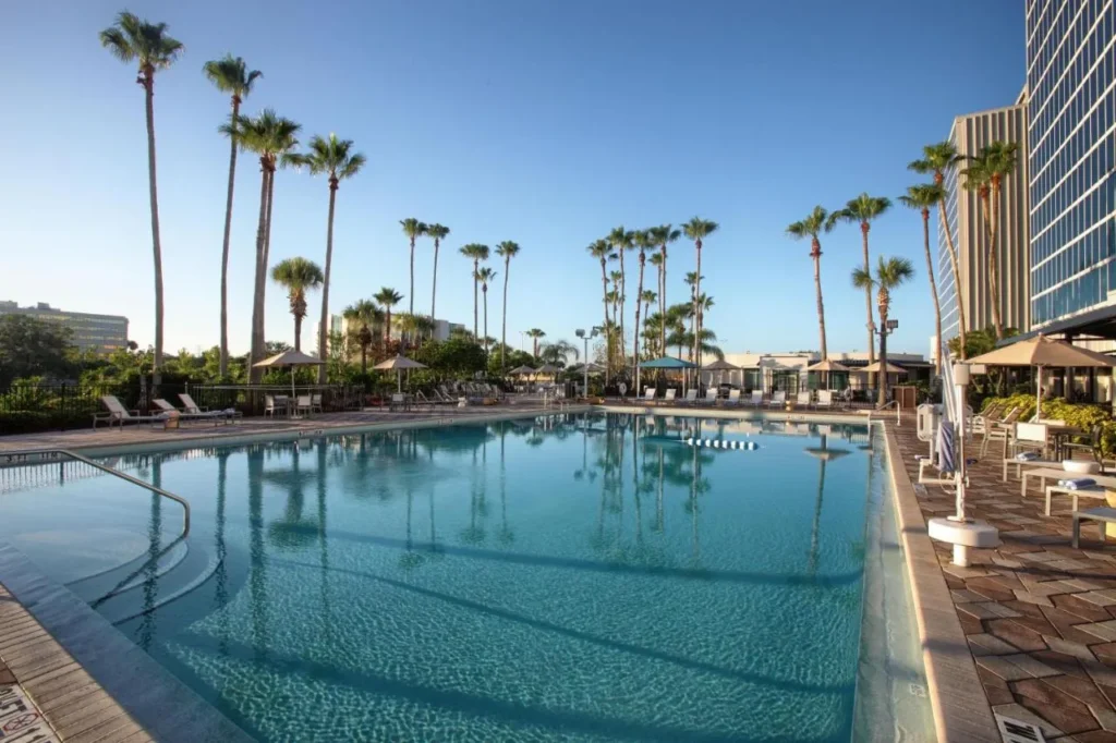 Piscina exterior bordeada de palmeras junto a la torre del hotel en DoubleTree at the Entrance to Universal