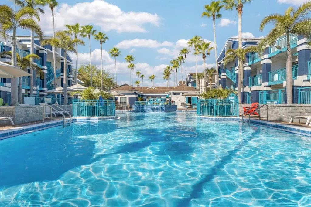 Piscina bordeada de palmeras entre edificios de suites azules y blancos en Sonesta ES Suites Lake Buena Vista