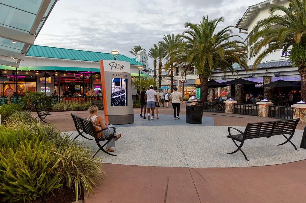 Plaza bordeada de palmeras con bancos, un letrero de directorio y restaurantes en Pointe Orlando en International Drive