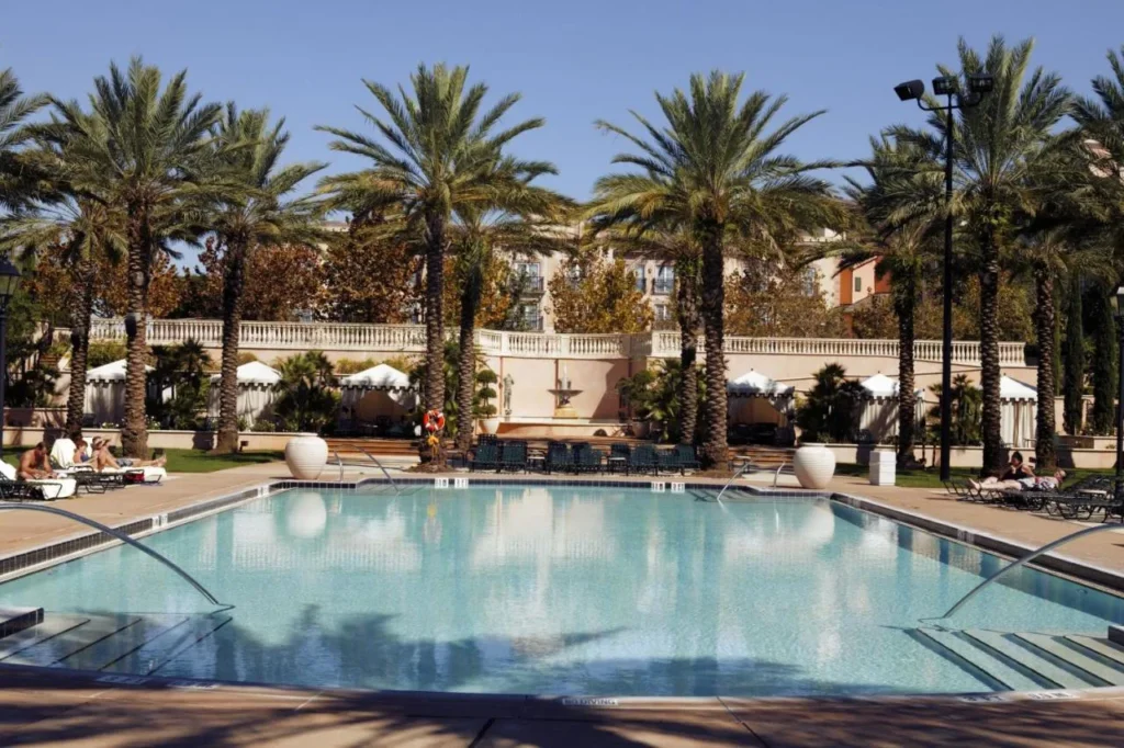 Palm-lined swimming pool with loungers and white umbrellas at Loews Portofino Bay Hotel
