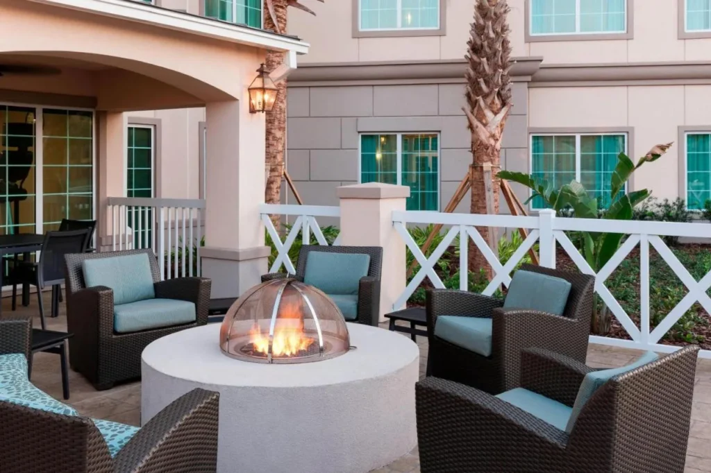 Patio de fogata con sillones de mimbre y palmeras fuera de Residence Inn Near Universal Orlando
