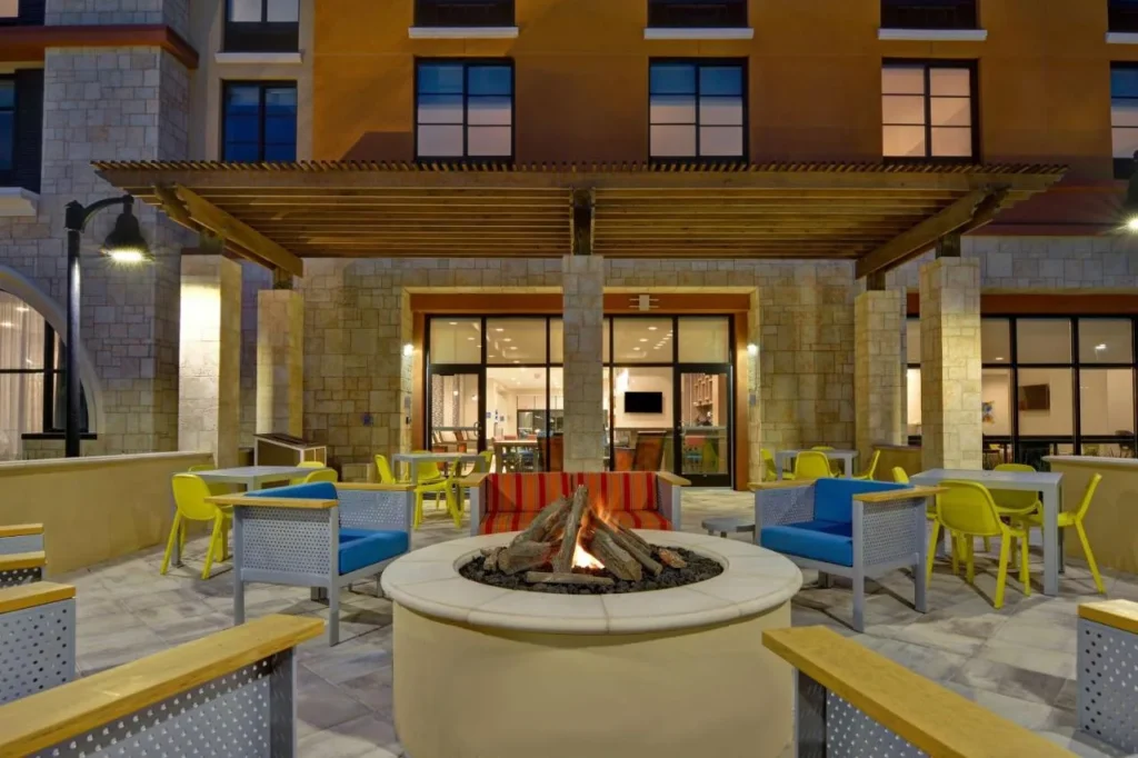 Patio con fogata redonda, sillas azules y una pérgola en el Home2 Suites Flamingo Crossings