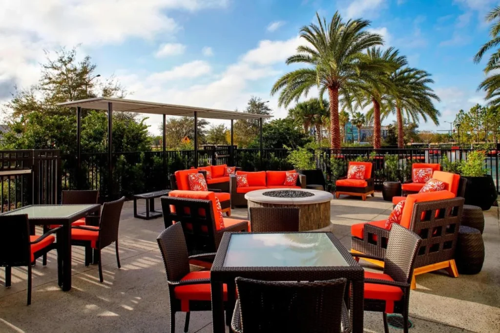Patio con fogata, asientos acolchados de color naranja y palmeras en el Residence Inn Orlando Lake Nona