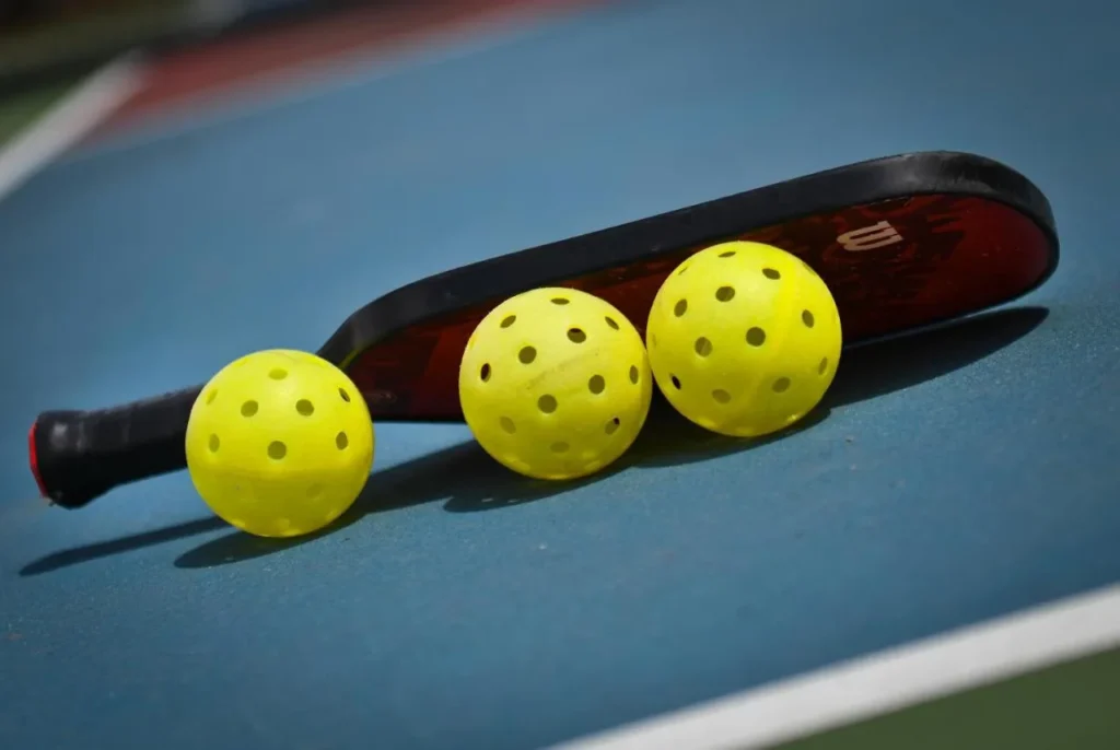 Pickleball paddle and three yellow balls on a blue court at Reunion Resort & Golf Club
