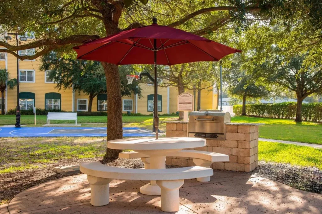 Mesa de picnic, sombrilla roja y parrilla junto a la cancha deportiva en el Residence Inn Orlando SeaWorld