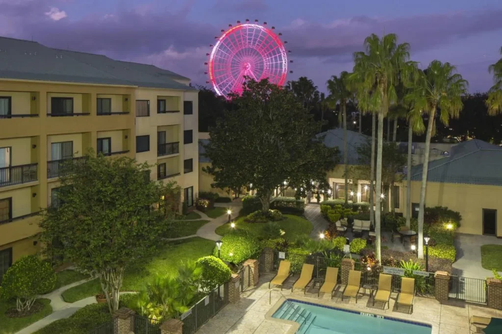Pool and gardens at dusk with The Orlando Eye lit pink behind Courtyard Orlando International Drive