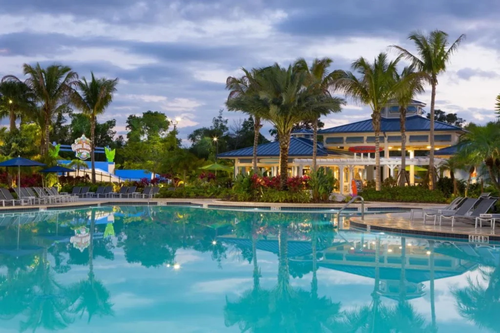 Piscina al atardecer con palmeras y un pabellón con techo azul en The Grove Resort
