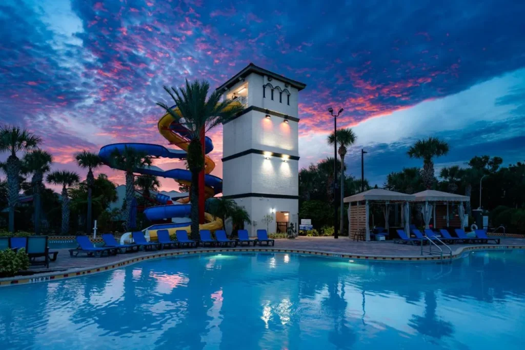 Piscina al atardecer con toboganes de agua retorcidos junto a una torre blanca en FantasyWorld Resort