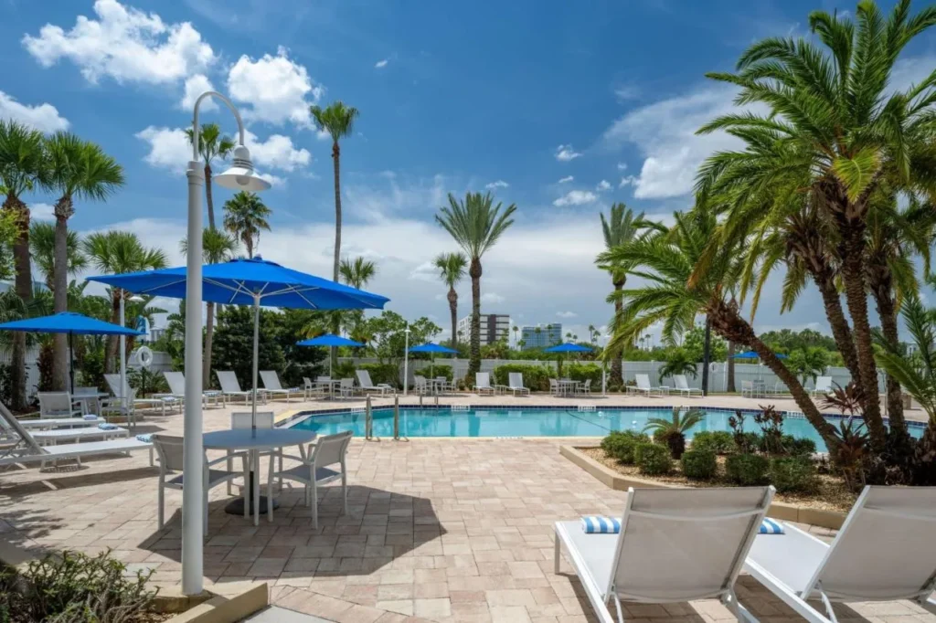 Cubierta de piscina con palmeras, sombrillas azules y tumbonas blancas en Four Points Orlando International Drive