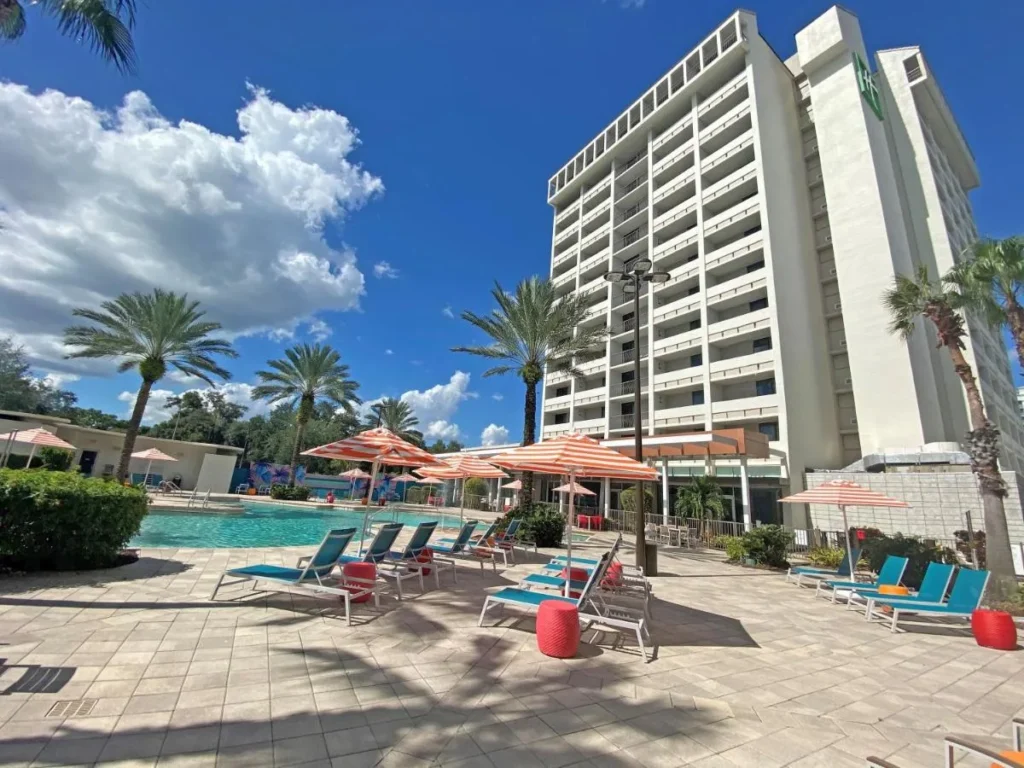 Pool deck with striped umbrellas below the tower of Holiday Inn Orlando &ndash; Disney Springs Area