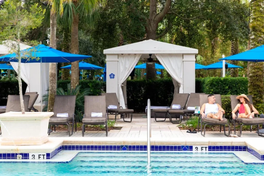 Pool edge with lounge chairs, blue umbrellas and a white curtained cabana at Omni Orlando Resort at ChampionsGate
