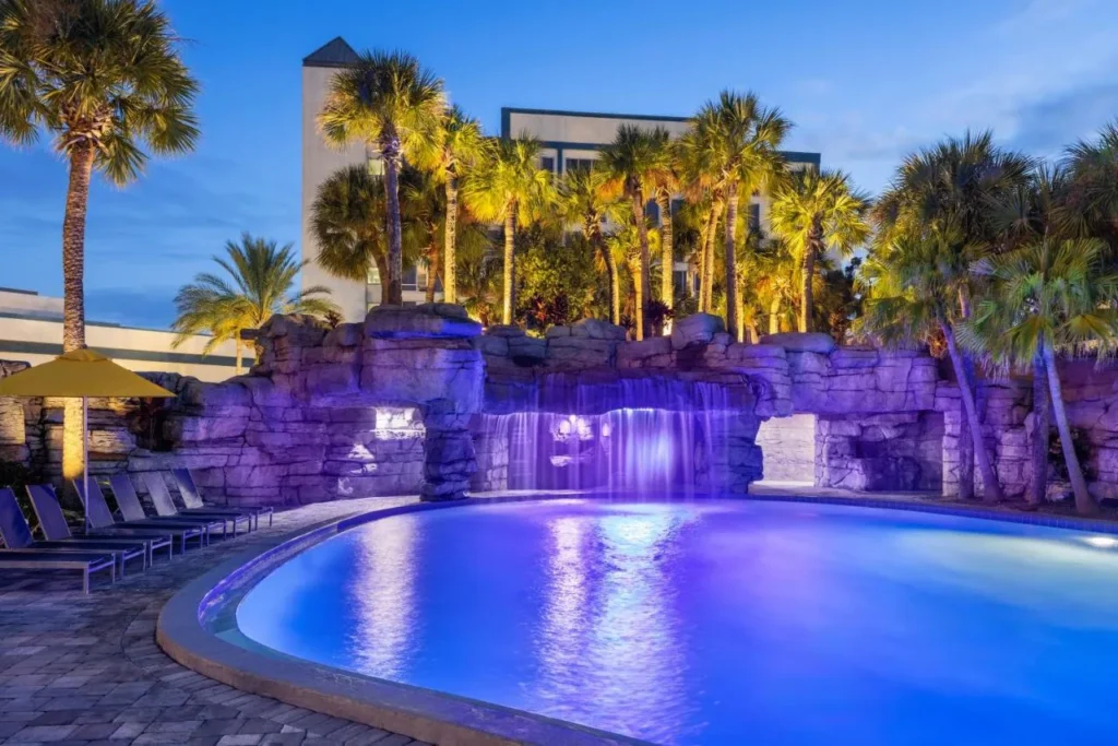 Piscina iluminada al atardecer junto a una gruta de cascada de roca en Delta Hotels Orlando Celebration