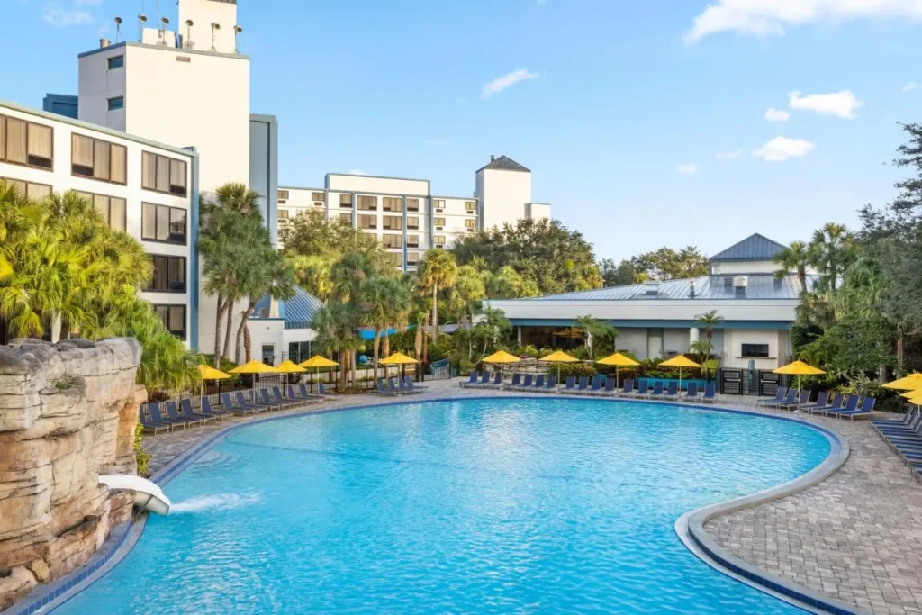 Piscina con cascada de roca y sombrillas amarillas junto a las torres en Delta Hotels Orlando Celebration