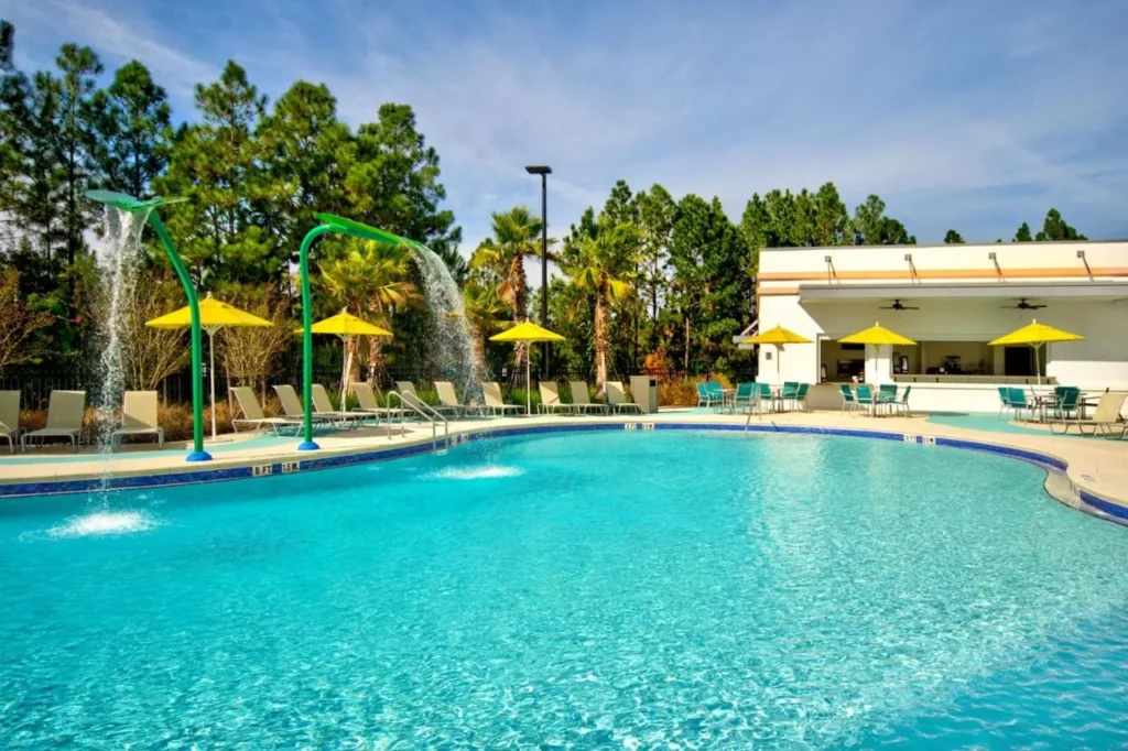 Piscina con chorros de fuente, sombrillas amarillas y bar cabaña en Fairfield Flamingo Crossings