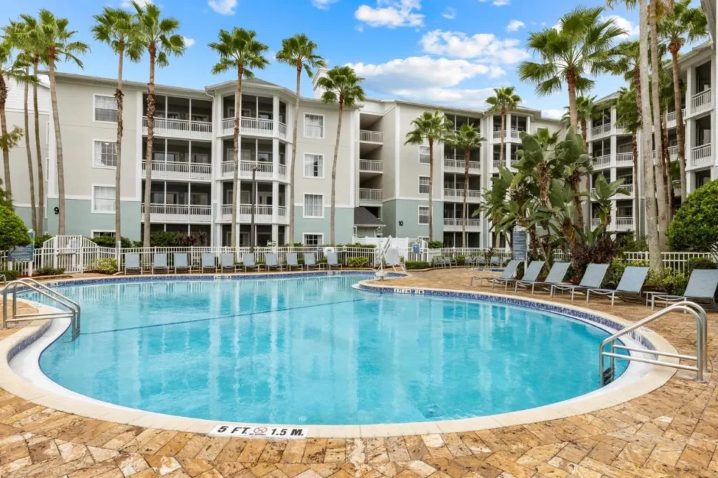 Pool with loungers in front of a four-story condo building at Club Wyndham Cypress Palms