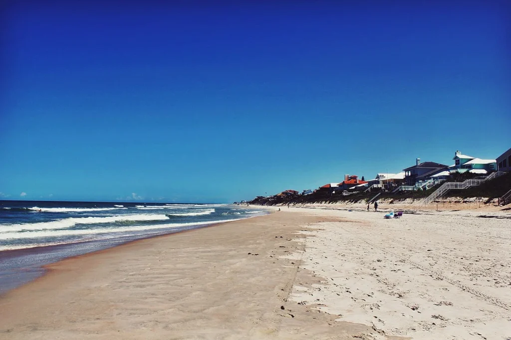 Tramo tranquilo de New Smyrna Beach con olas, arena suave y casas de playa a lo largo de las dunas