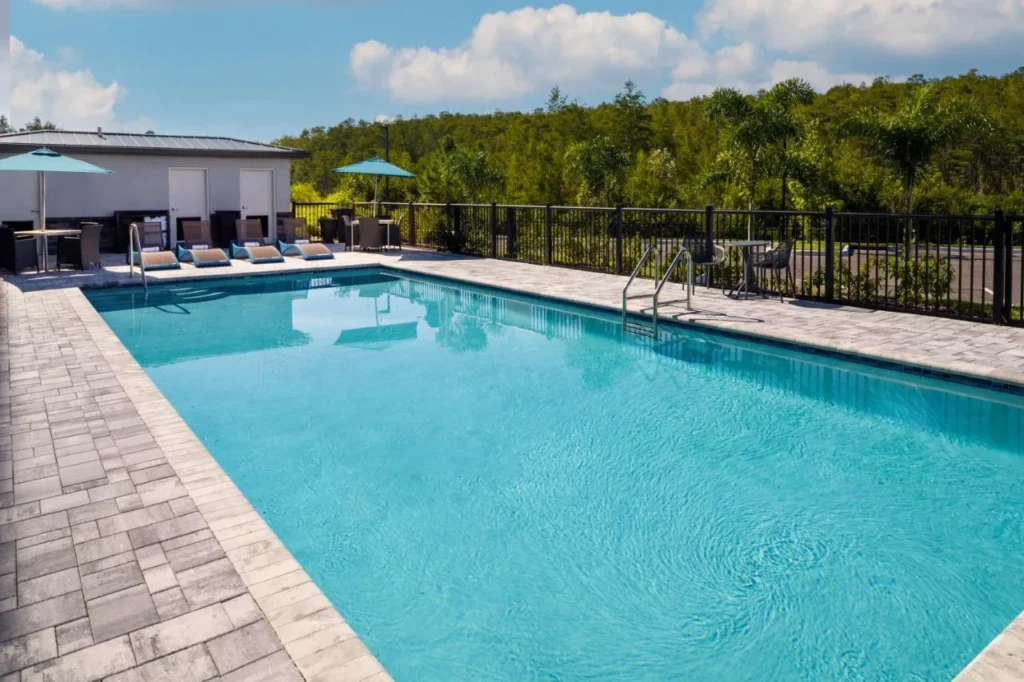 Piscina exterior rectangular con tumbonas y sombrillas azules en Hampton Inn Kissimmee North