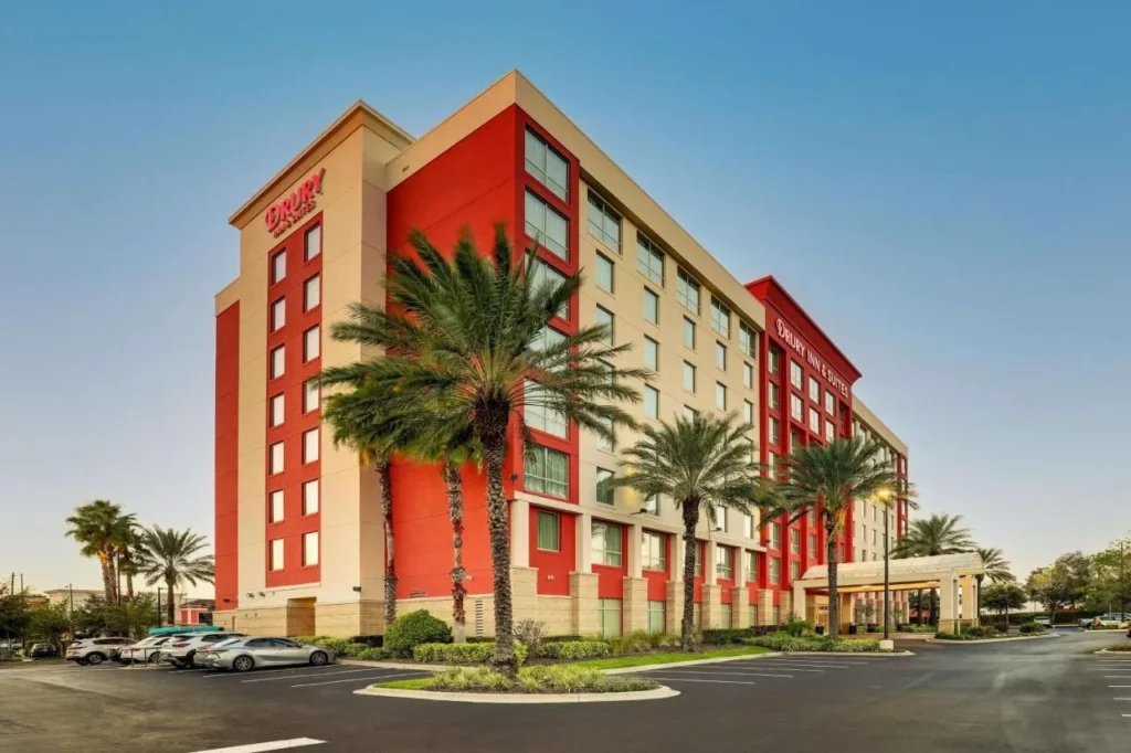 Exterior en rojo y blanco con palmeras y estacionamiento de Drury Inn and Suites cerca de Universal Orlando