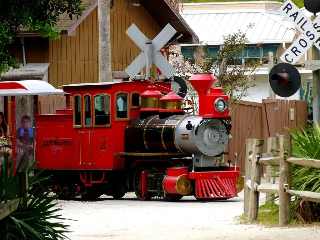 Red Gatorland Express steam-style train passing a railroad crossing sign inside Gatorland Orlando