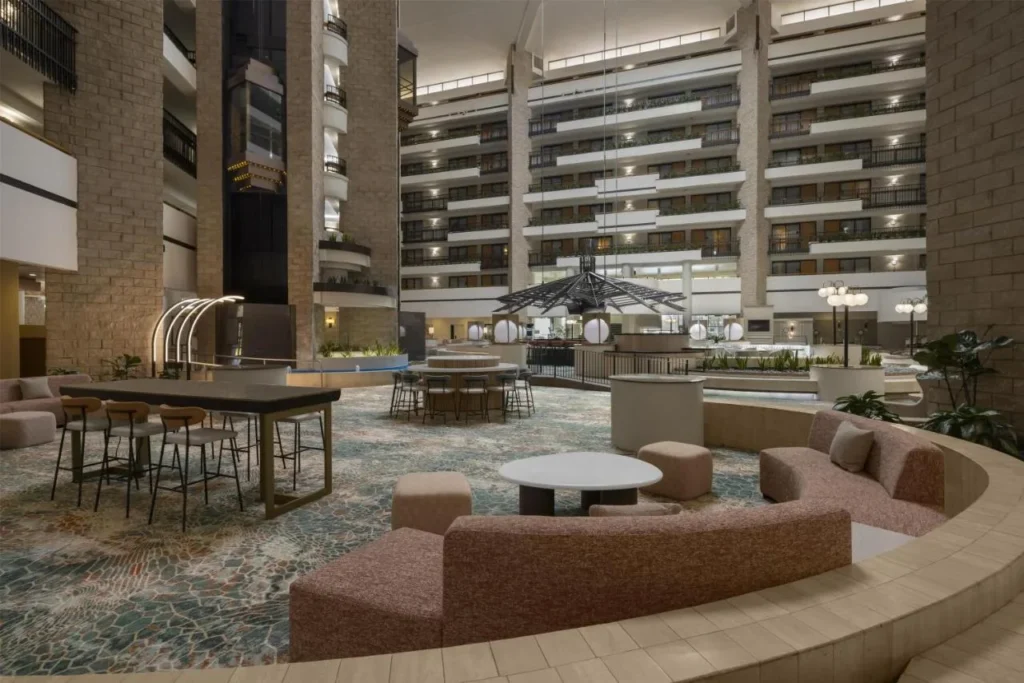 Sal&oacute;n en el atrio renovado con sof&aacute; curvo, mesas altas y balcones arriba en Embassy Suites ICON Park