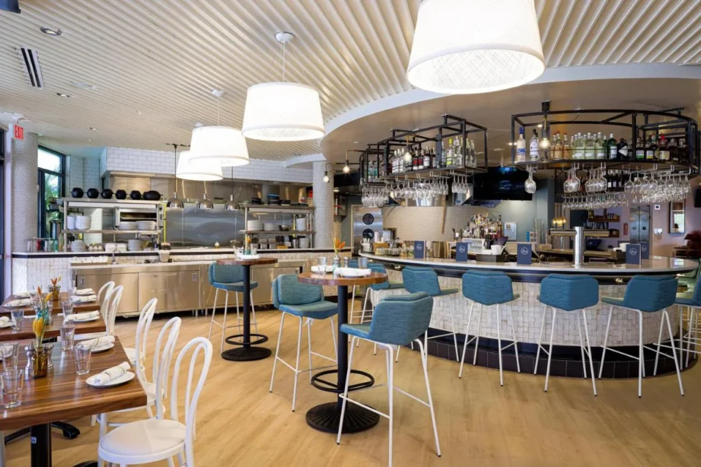 Bar restaurante con taburetes azules, lámparas colgantes blancas y una cocina abierta en Meliá Orlando Celebration