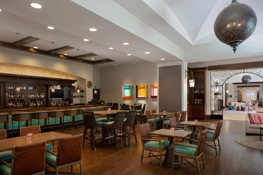 Restaurant bar with teal-cushioned chairs and dining tables at The Alfond Inn