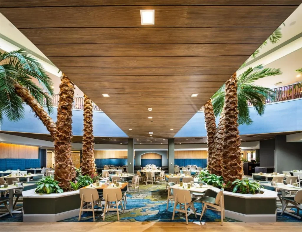 Restaurant tables between tall palm trunks in the atrium at Caribe Royale Orlando