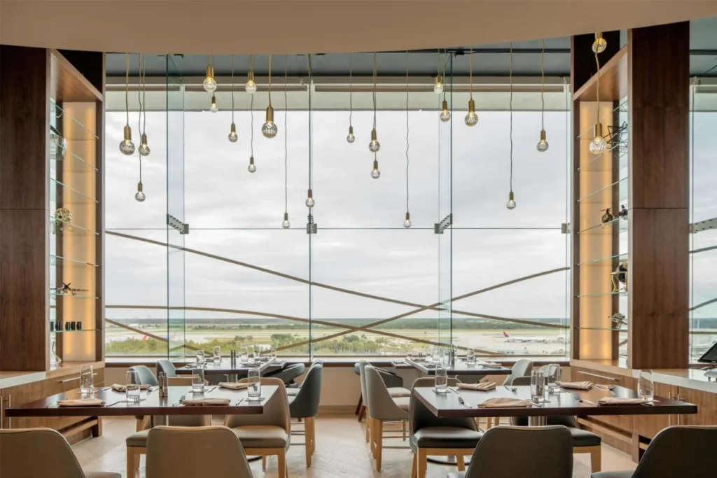 Mesas de restaurante frente a ventanas altas con vistas al aer&oacute;dromo en el Hyatt Regency Orlando International Airport
