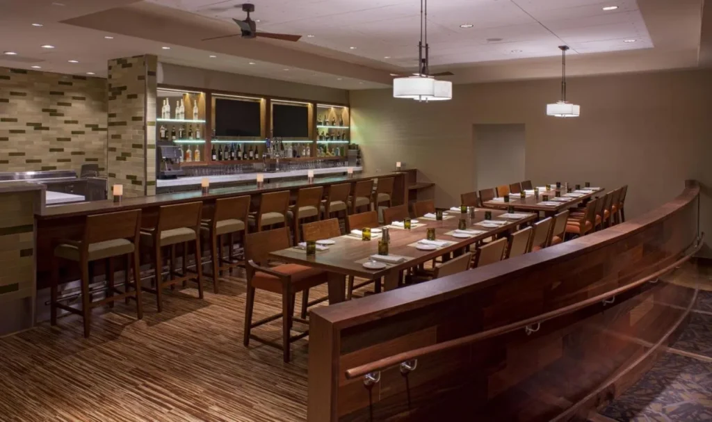 Restaurante con bar retroiluminado y mesas largas de madera en el Hyatt Regency Orlando International Airport
