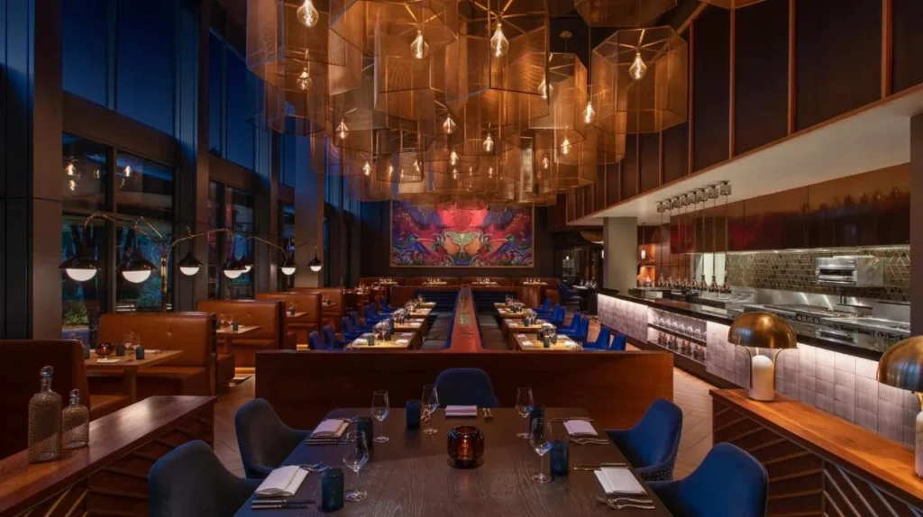 Restaurante con cocina abierta, faroles de cobre y un colorido mural en el Lake Nona Wave Hotel