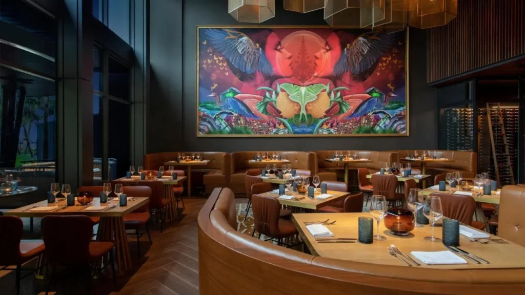 Restaurante con cabinas de cuero curvadas debajo de un gran mural colorido en Lake Nona Wave Hotel