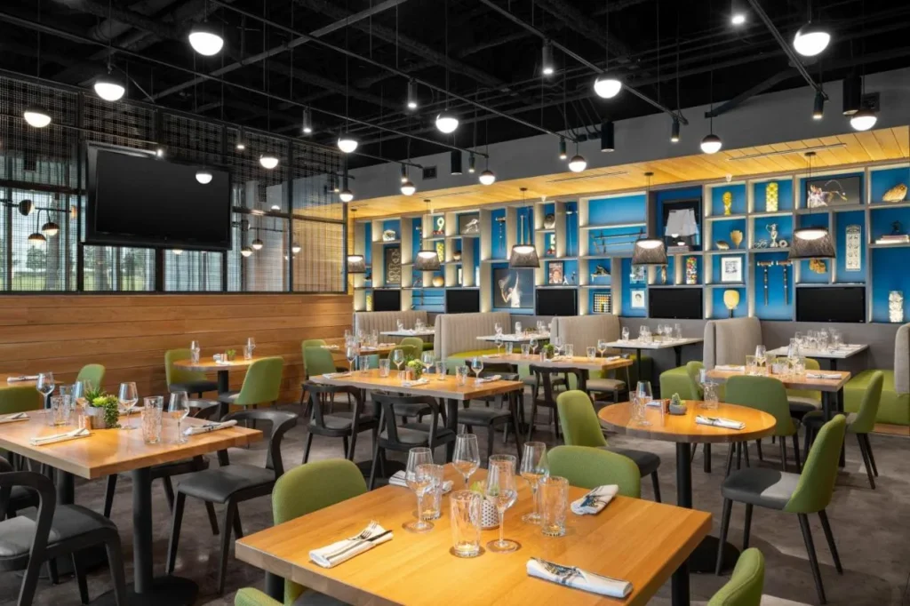 Restaurante con sillas verdes, mesas de madera y estantes de recuerdos de tenis en el Aloft Orlando Lake Nona