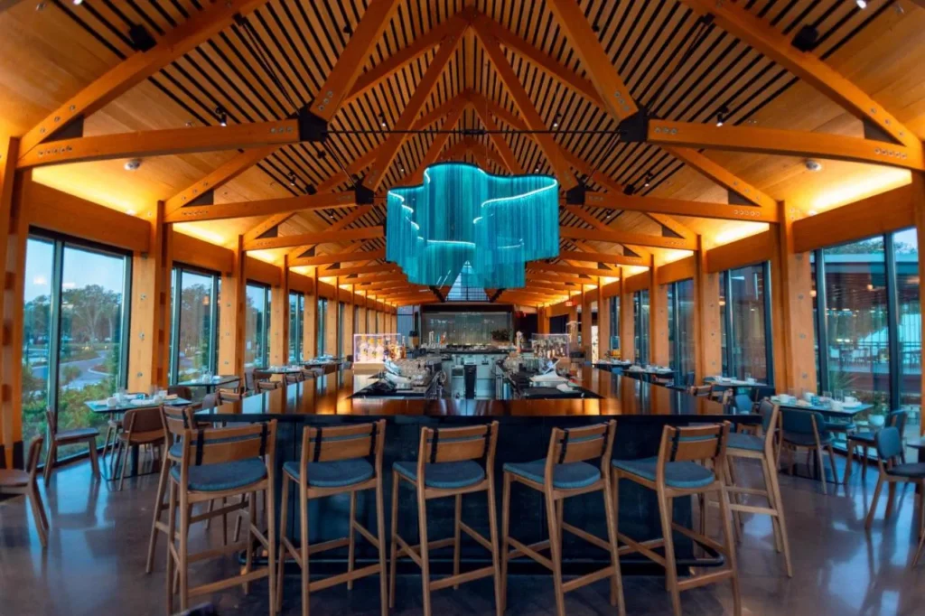 Restaurant with timber-truss ceiling, long bar and blue glass chandelier at Evermore Orlando Resort