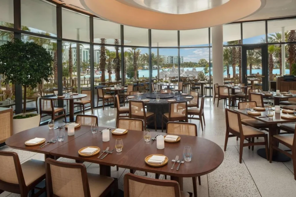 Restaurante con sillas de madera y rat&aacute;n y paredes de vidrio frente a Evermore Bay en Conrad Orlando