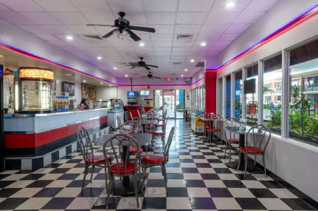 Restaurante retro con piso a cuadros, sillas rojas y mostrador de pizza en Ramada by Wyndham Kissimmee Gateway