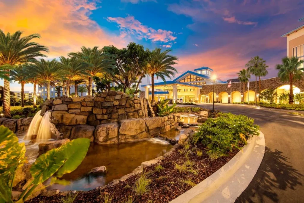 Cascada de roca y entrada bordeada de palmeras que conduce a la entrada en Loews Sapphire Falls Resort