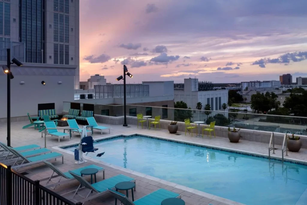 Piscina en la azotea al atardecer con tumbonas turquesas y fogata en Hilton Garden Inn Orlando Downtown