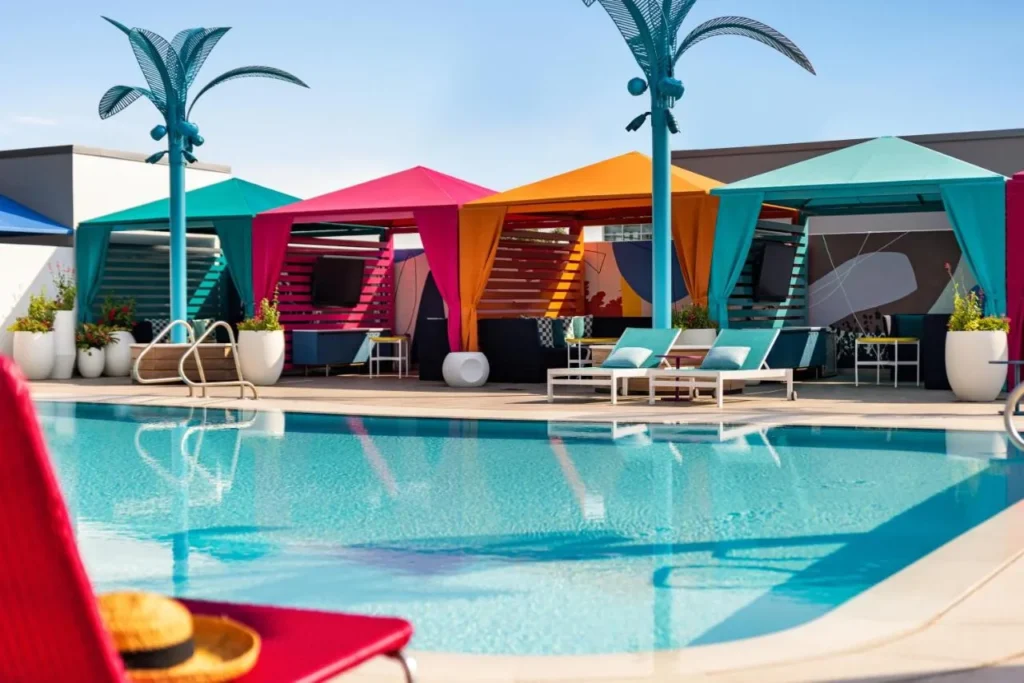 Piscina de olas en la azotea con coloridas caba&ntilde;as con cortinas y esculturas de palma de metal en Lake Nona Wave Hotel