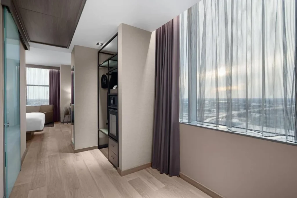 Entrada a la habitación con armario, caja fuerte, mini nevera y una amplia ventana en AC Hotel Orlando Downtown