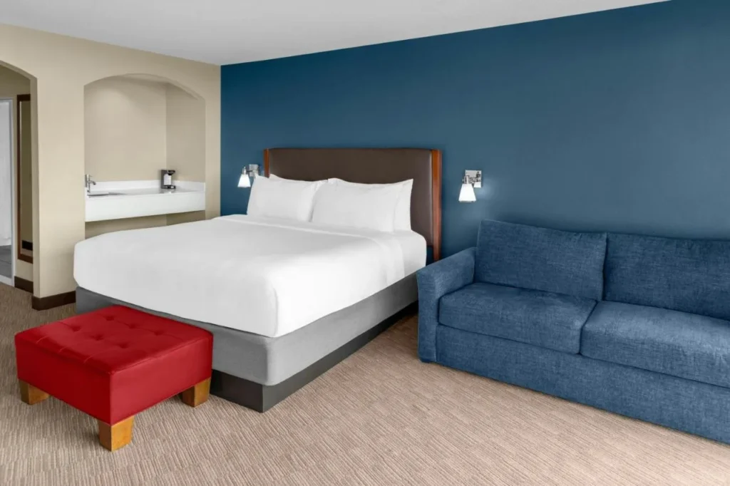 Habitación con cama grande, sofá azul y lavabo con barra húmeda en Four Points Orlando International Drive