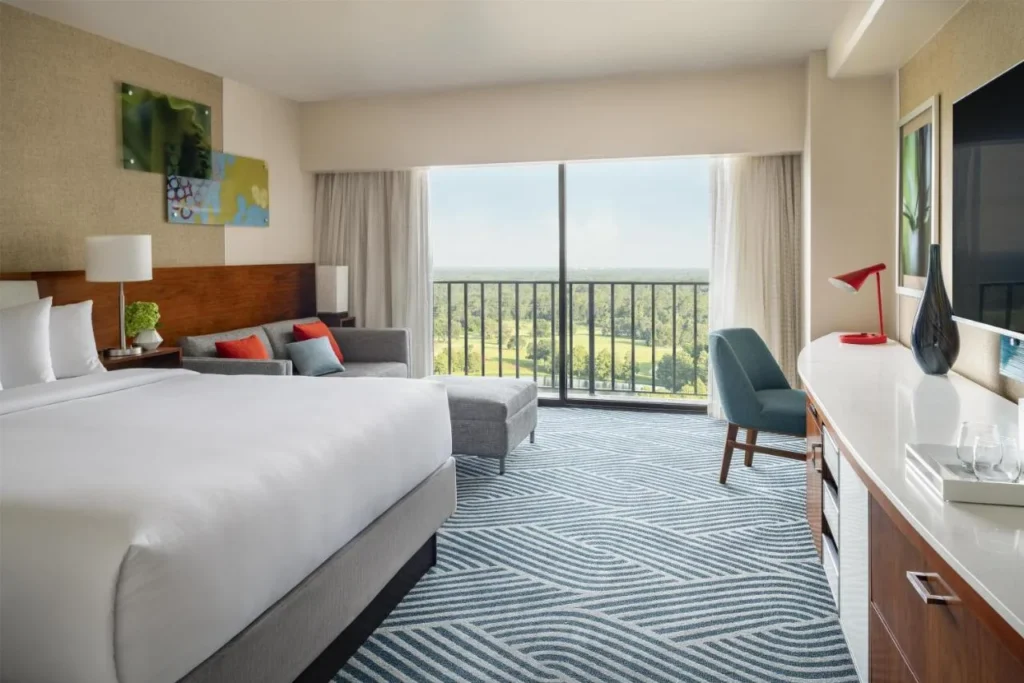 Room with a large bed, sofa and balcony over green grounds at Hyatt Regency Grand Cypress